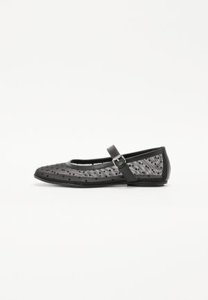 Chaussure plate noire avec un bout arrondi, présentant un dessus en mesh à pois et une bride avec une boucle sur le côté.