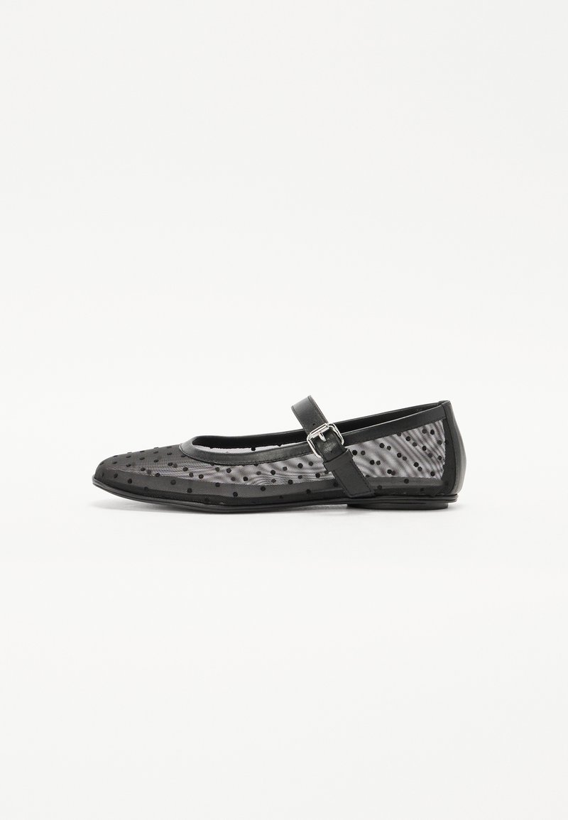 Black flat shoe with a rounded toe, featuring a mesh upper with polka dots and a strap with a buckle on the side.