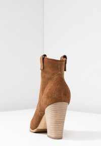 Botte chelsea en suede marron avec un bout rond, un talon en bois empilé et des détails cousus. Comprend des languettes de tirage et un talon texturé pour un meilleur maintien.