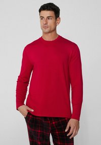 Camisa roja de manga larga hecha de una tela suave, con un escote redondo. Combinada con pantalones de pijama a cuadros en negro y rojo.