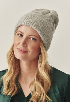 Grijze gebreide beanie met een geribbelde textuur en een slouchy ontwerp. Zachte wol en subtiele patroondetails zijn zichtbaar.