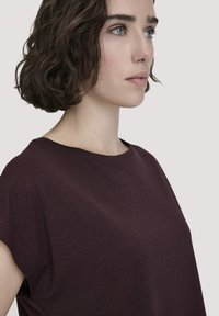 Burgunderfarbenes Kurzarmtop mit rundem Ausschnitt, das eine weiche Textur und einen lässigen Schnitt aufweist. Ein seitlicher Schlitz verleiht dem Design eine besondere Note.