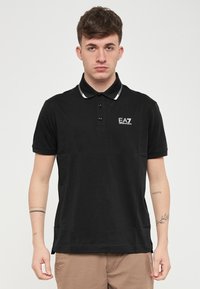 Polo shirt nera in cotone, con apertura a due bottoni, dettagli a righe bianche sul colletto e logo sul petto.
