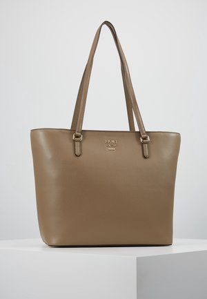 Sac fourre-tout en cuir couleur taupe de DKNY avec deux anses d'épaule, présenté sur un piédestal blanc contre un fond neutre.