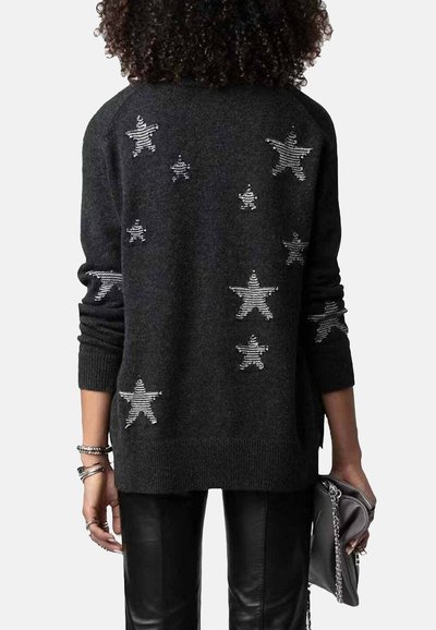 Pull noir à coupe décontractée, orné d'embellissements en forme d'étoiles argentées et de poignets côtelés. Porté avec un pantalon en cuir et une pochette.