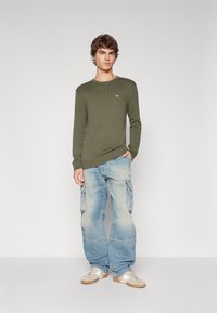 Pull en tricot côtelé vert olive à manches longues, associé à un jean cargo baggy bleu clair avec des poches latérales et une finition délavée.