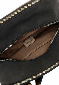 Zwarte stoffen handtas met gouden ritsdetails, voorzien van een bruine binnenkant, een extra vak en een gestructureerd label aan de binnenzijde.