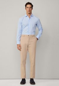 Camisa de cuadros azul claro con mangas largas, combinada con chinos beige y zapatos azul oscuro. Diseño ajustado, detalle de botones en la camisa.
