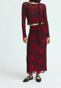 Haut à manches longues en dentelle florale noire avec boutons, associé à une jupe florale noire assortie. La tenue est ornée d'un nœud décoratif et présente une texture douce.