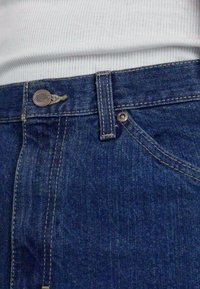 Jeans i denim med knappelukking, lys søm og midjehøyde. Stoffet har en mørkeblå farge med en glatt tekstur.