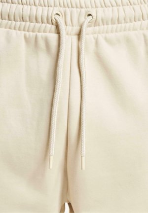 Beige sweatpants med elastisk talje og snøre. Glat overflade og enkelt design med metaløjer til snøret.