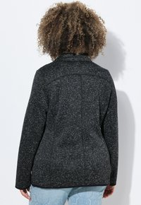 Giacca nera con texture, colletto alto, maniche lunghe e una silhouette sartoriale. Caratterizzato da un notevole motivo a macchie grigie chiare su tutta la superficie.