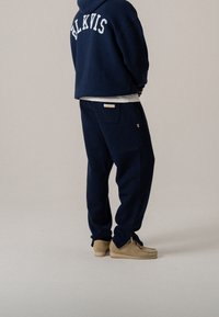 Marineblauwe oversized hoodie met witte "BLKVIS" letters, gecombineerd met bijpassende tapered broek met zijritsen en beige instappers.