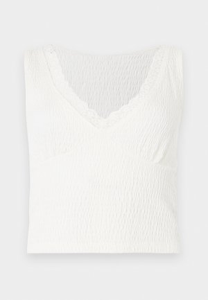 Haut sans manches texturé blanc avec encolure en V et délicate bordure en dentelle autour du cou, présenté sur un fond uni.