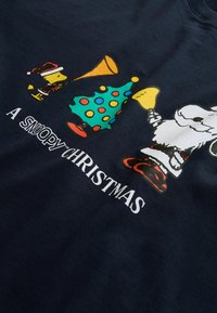 Tumesinine t-särk, millel on Snoopy ja Woodstocki joonistused, värvikas punktidega jõulupuu ning valge tekst "Jõulud Snoopyga".