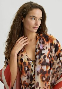 Luipaardprint kimono van zijden stof, met oranje, bruin en crème tinten. Vloeiende mouwen met rode accenten, lichtgewicht en doorschijnende textuur.