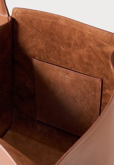 Intérieur en daim marron d'un sac à main en cuir avec une poche intérieure cousue et une petite étiquette de marque embossée.