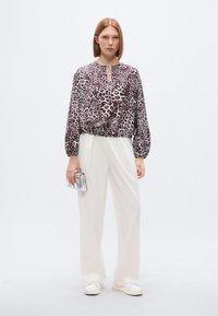 Μπλούζα με λεοπάρ σχέδιο, λαιμόκοψη με άνοιγμα, ζωνάκι στη μέση και μακριά μανίκια· συνδυασμένη με άνετο λευκό παντελόνι και ασημένιο τσαντάκι χειρός.