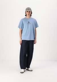 Light blue cotton t-shirt with a round neck and printed logo, paired with dark navy striped wide-leg pants and white sneakers.