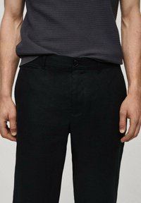 Pantaloni neri con una texture liscia, dotati di chiusura a bottone, passanti per cintura e tasche laterali. Taglio dritto.