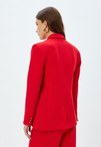 Rode op maat gemaakte blazer met lange mouwen, een gladde textuur en gouden knoopaccenten op de mouwen. Heeft een klassieke kraag en een getailleerde pasvorm.