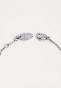 Silverkedjearmbandslås med oval etikett prydd med präglad orb och korslogotyp på vit bakgrund.