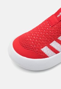 Roter Sportschuh mit atmungsaktivem Strick-Obermaterial, glattem roten Gummikappe, weißem Drei-Streifen-Design und weißer Sohle.