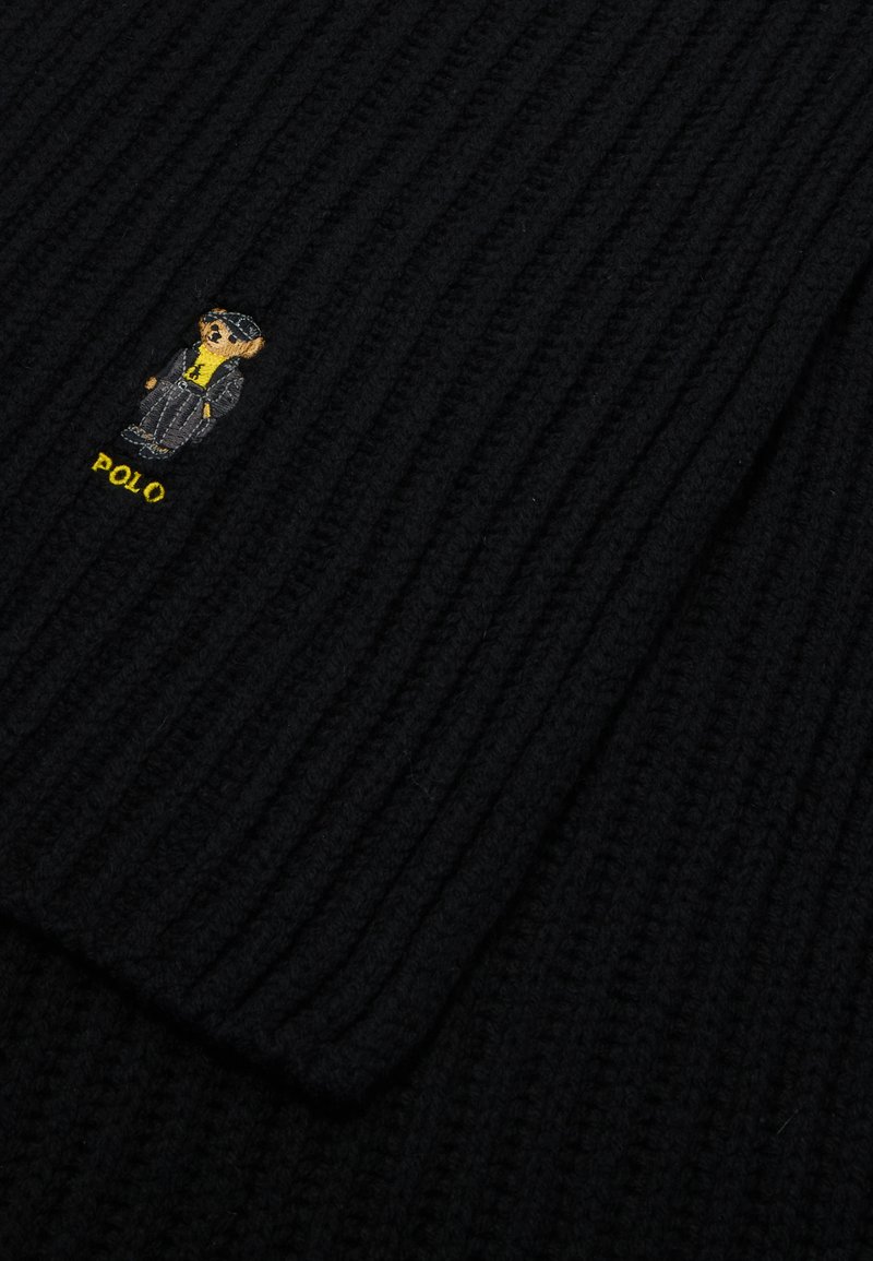 Pull en maille côtelée noir avec un petit ours brodé portant un costume gris et une chemise jaune, avec le texte "POLO" en jaune en dessous.