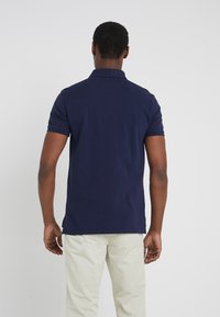 Granatowa koszulka polo z kołnierzykiem i krótkimi rękawami, wykonana z teksturowanej tkaniny. Tył ma boczne rozcięcia dla większego komfortu.