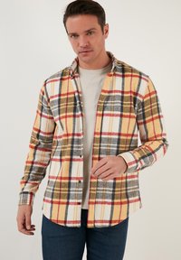 Flanellen shirt met een gele, rode, zwarte en witte ruitpatroon, knoopsluiting kraag en een effen lichtgekleurde ondershirt.