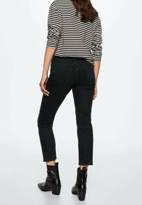 Mustat kapeat farkut, joiden kanssa on yhdistetty raidallinen pitkähihainen paita. Farkuissa on klassinen viiden taskun muotoilu ja ne ulottuvat nilkkapituuteen. Mustat nilkkurit viimeistelevät ilmeen.