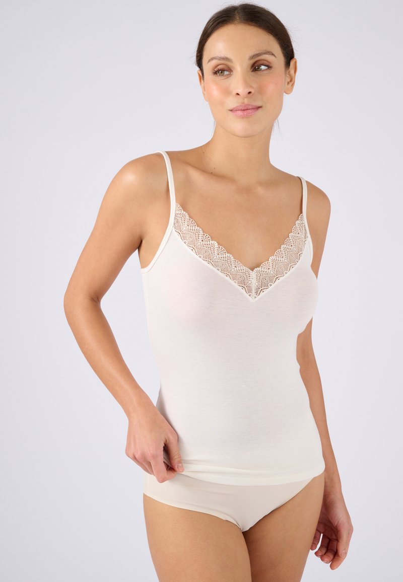 Top bianco senza maniche con bordo in pizzo lungo il collo a V, spalline sottili e un design aderente, indossato con biancheria intima beige coordinata. Texture liscia.