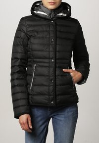 Sorte quiltede pufferjakke med hætte, der har trykknapper, lynlåslommer på siderne og grå indvendig foring.