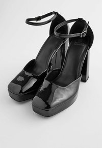 Escarpins plateformes en cuir verni noir avec un bout carré, une bride de cheville et un talon bloc épais. Texture lisse avec une finition brillante.