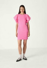 Vestido bodycon rosa com mangas bufantes curtas, decote redondo e comprimento até aos joelhos. Usado com sapatos planos pretos e meias brancas até ao tornozelo.