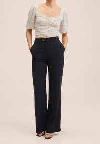 Hvid cropped top med puffærmer, prikket mønster; parret med højtaljede sorte bukser; har sidelommer, glat tekstur og lige ben.