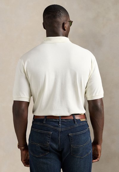 Lys gul polo med klassisk krage, korte ermer og glatt tekstur, kombinert med mørkeblå denimjeans.