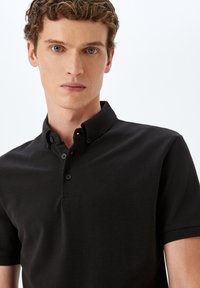Svart polo skjorta med en strukturerad tyg, med krage, knäppning med tre knappar och korta ärmar. Ren design utan mönster.