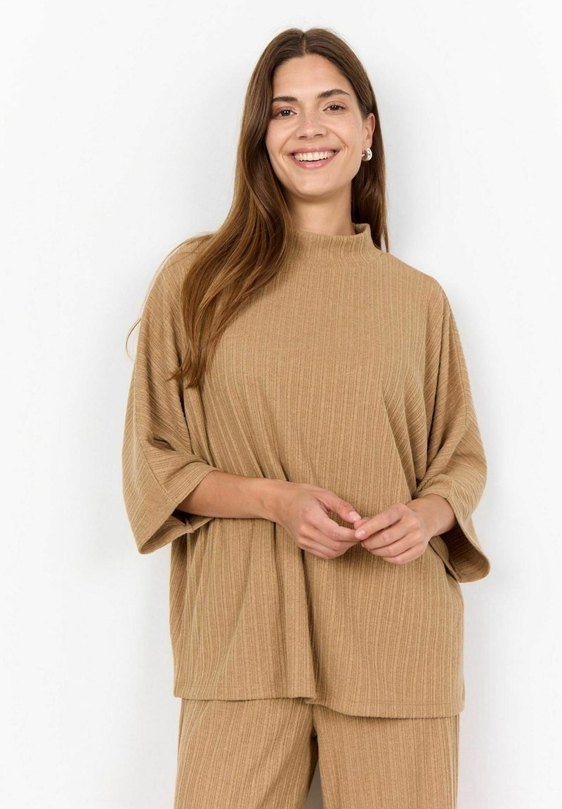 Tana rebrasta oversized majica s visokim ovratnikom i širokim rukavima, napravljena od mekog materijala, u kombinaciji s odgovarajućim donjim dijelom.