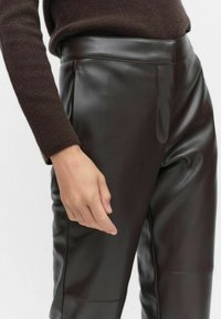 Bruine leren broek met een gladde textuur, hoge taille en zijzakken. De stof heeft een lichte glans, wat mooi samengaat met een gebreide donkerbruine top.