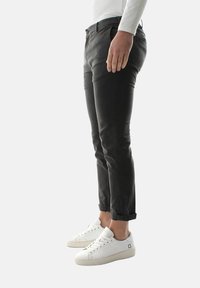 Pantaloni in cotone grigio scuro con vestibilità slim, orli arrotolati e una texture liscia; abbinati a sneakers bianche con dettagli perforati.