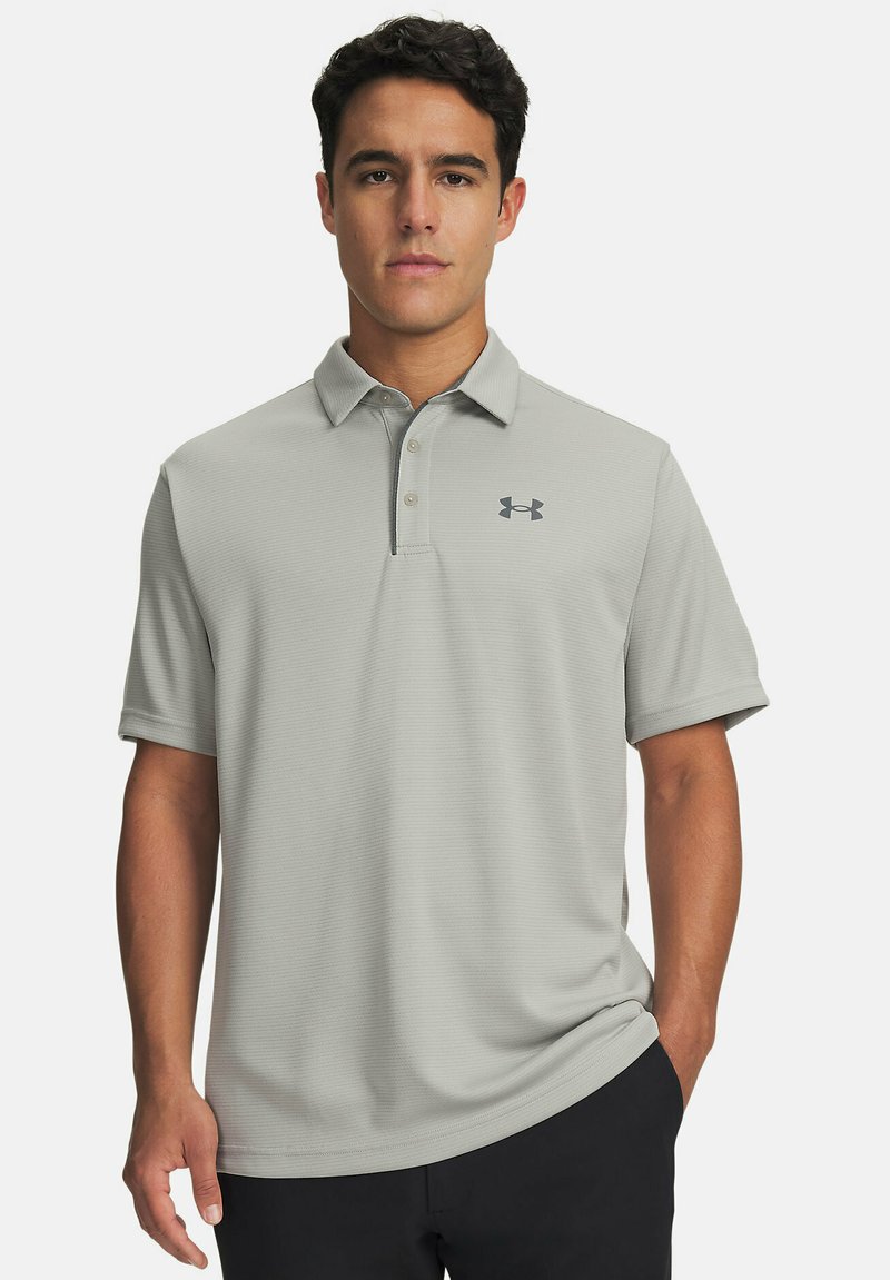 Polo gris clair à manches courtes, patte de boutonnage à trois boutons, avec le logo Under Armour en gris foncé. Tissu texturé avec un motif subtil.