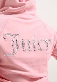 Roze hoodie gemaakt van zachte stof, met een groot met rhinestones versierd "Juicy" logo op de rug, voorzien van een ontspannen pasvorm en capuchon.