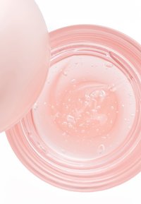 Conteneur en verre rose transparent avec un liquide tourbillonnant et des bulles visibles, doté de bords lisses et d'un design arrondi et minimaliste.