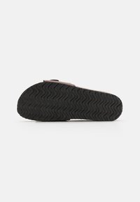 Svart gummisåle til sandaler med et sikksakk-mønster, med en brun såle og et minimalistisk design.