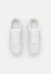 Ein Paar weiße und hellgraue Sneakers mit perforierten Zehenkappen, weißen Schnürsenkeln und beigen Fersenakzenten, von oben auf einem weißen Hintergrund betrachtet.