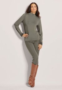 Olivgrünes Langarmoberteil mit hohem Kragen und Pailletten-Ärmeldetails, kombiniert mit olivfarbenen Leggings und knielangen braunen Lederstiefeln.