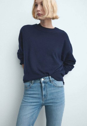 Pull oversize bleu marine en tissu doux, associé à un jean taille haute bleu clair. Coupe décontractée avec manches retroussées et accents minimalistes.