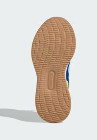 Gummisohle mit einem strukturierten, wellenförmigen Muster. Farbe: hellbraun mit Rillen für bessere Haftung. Der Rand hat einen blauen und gelben oberen Abschnitt.