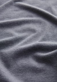 Tissu en coton gris avec une texture douce, présentant des plis naturels et des variations de ton subtiles à la surface.